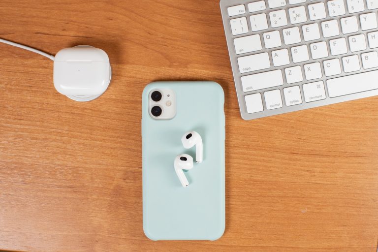 AirPods case on a MagSafe charger (left), AirPods on top on iPhone (middle), and a keyboard (right).