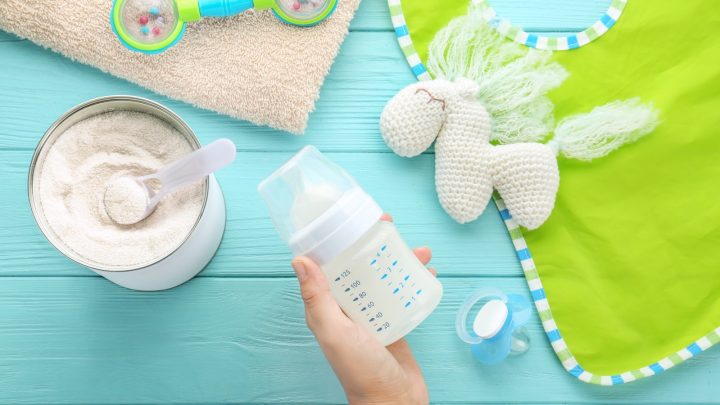 Woman holding feeding bottle of baby milk formula on wooden background