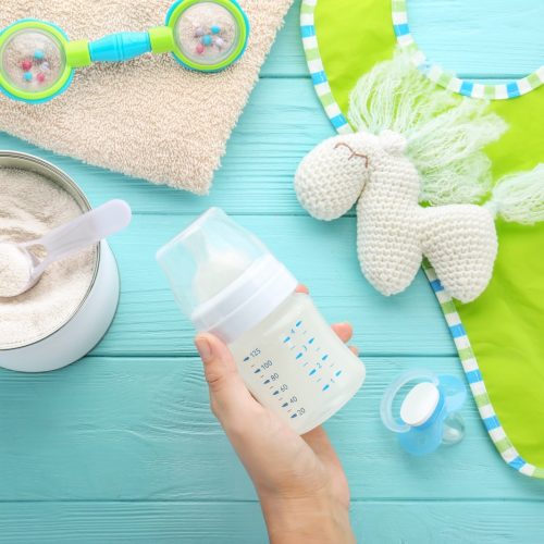 Woman holding feeding bottle of baby milk formula on wooden background