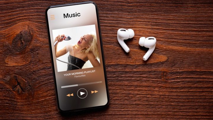 AirPods Pro 2 Features Music player on screen of iPhone and AirPods Pro on wooden surface.