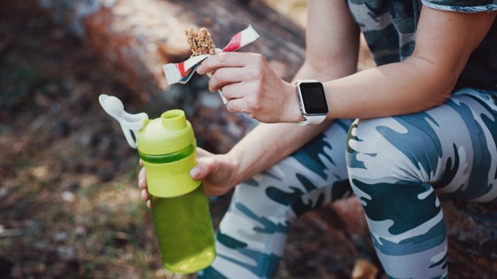 A woman eating a protein bar and hydrating during exercise.