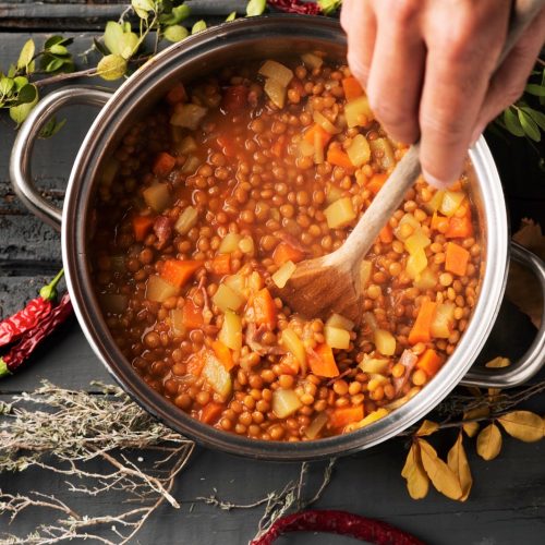 A person preparing a vegetarian lentil soup.